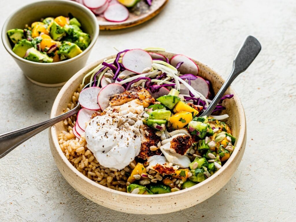 Nutritionally-balanced burrito bowl with fish, brown rice, radish, cabbage, mango avocado salsa, Greek yoghurt and seeds – a nutrient-rich meal for perimenopause and menopause nutrition.