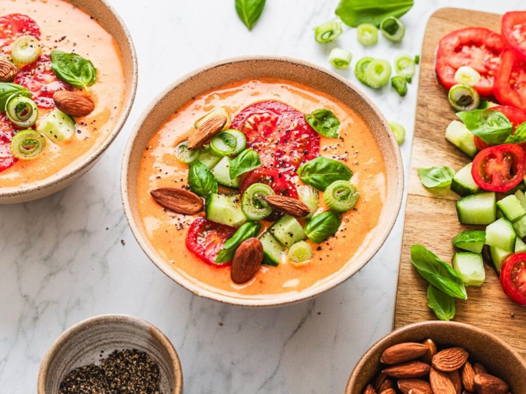 Bowl of gazpacho topped with fresh tomato, cucumber, almonds and basil – a Mediterranean-style heart-healthy recipe for perimenopause and menopause nutrition.