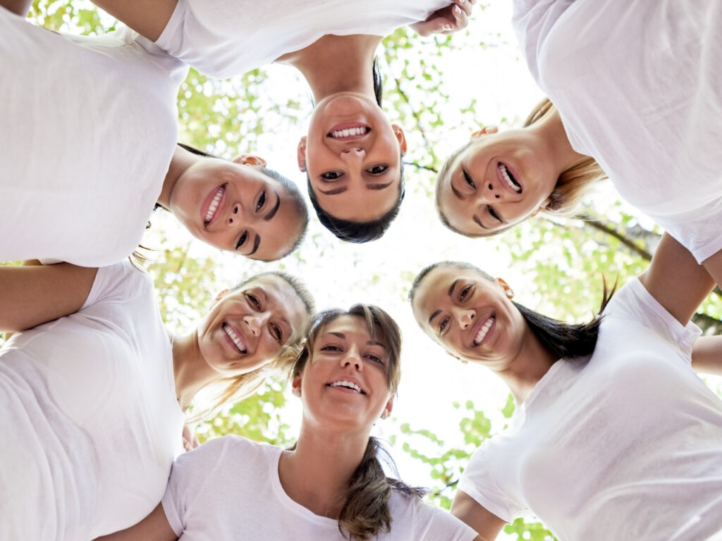 Women standing in a supportive circle smiling down at the camera, symbolising community connection for brain health in perimenopause.