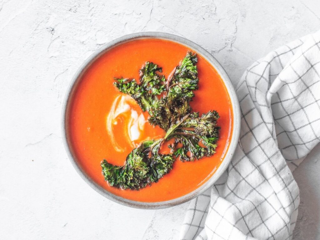 Bowl of vibrant roast tomato and red pepper soup topped with crispy kale, rich in vitamin C to support brain health during perimenopause.